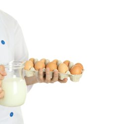 Young chef holds eggs and milk, isolated on white background